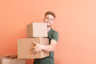 Young man with cardboard boxes on color background