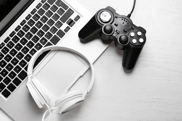 Laptop moderno, almofada de jogo e fones de ouvido na mesa de madeira — Fotografia de Stock