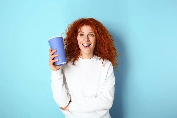 Beautiful redhead woman with drink on color background