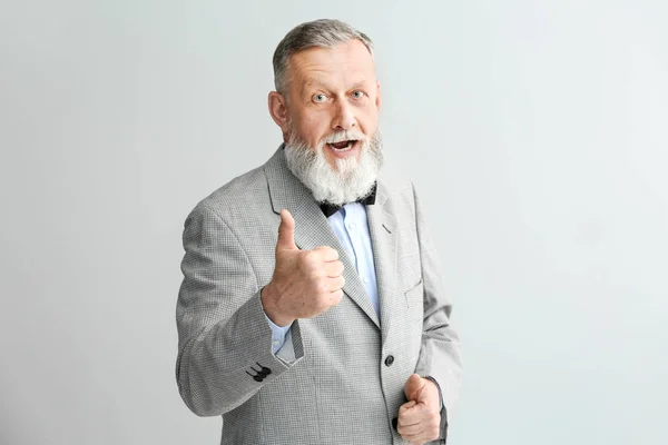 Portrait of handsome senior man showing thumb-up gesture on light background — Stock Photo, Image