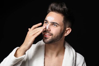 Yakışıklı adam karanlık arka plan karşı yüzüne kil maskesi uygulayarak