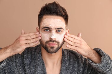 Yakışıklı adam renkli arka plan karşı yüzüne kil maskesi uygulayarak