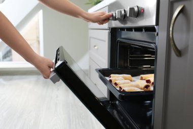 Woman taking baking tray with homemade pastry out of oven