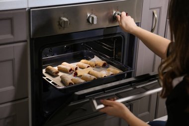 Woman taking baking tray with homemade pastry out of oven