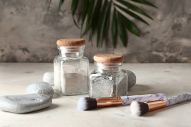 Jars with cosmetic clays, stones and brushes on table clipart