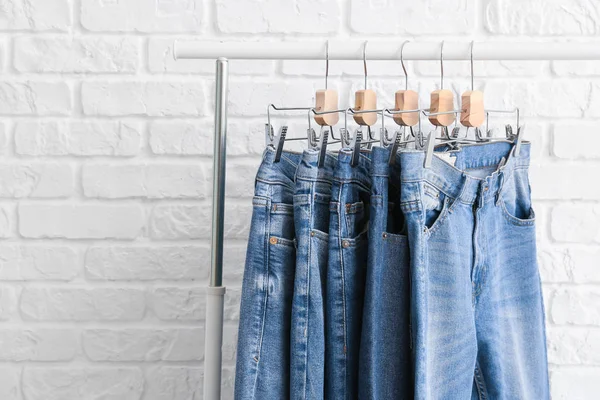 Perchero con diferentes pantalones vaqueros con estilo sobre fondo de ladrillo blanco —  Fotos de Stock