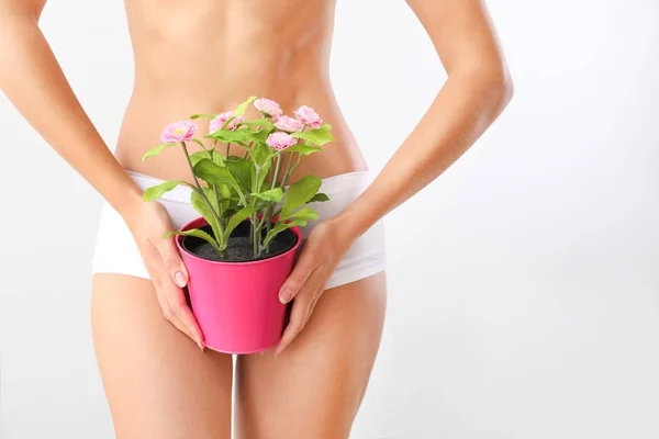 Mooie jonge vrouw met plant in pot op lichte achtergrond. Ontharing concept — Stockfoto