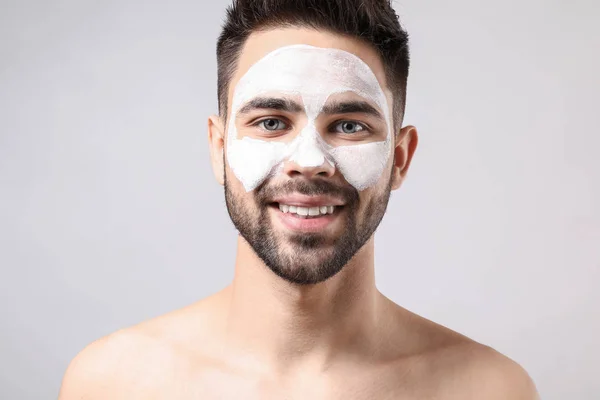 Handsome man with clay mask on his face against light background — Stock Photo, Image