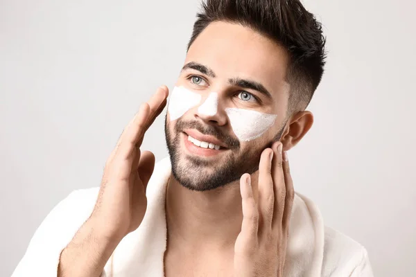 Hombre guapo con arcilla cosmética en su cara contra fondo claro — Foto de Stock