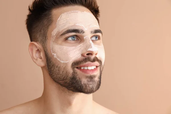 Knappe man met klei masker op zijn gezicht tegen kleur achtergrond — Stockfoto