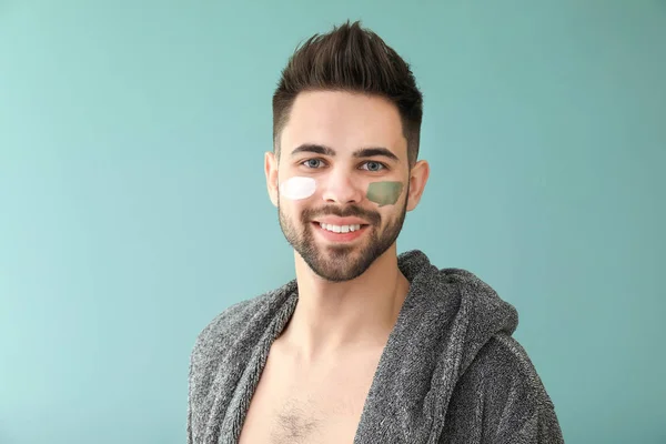 Handsome man with cosmetic clay on his face against color background — Stock Photo, Image