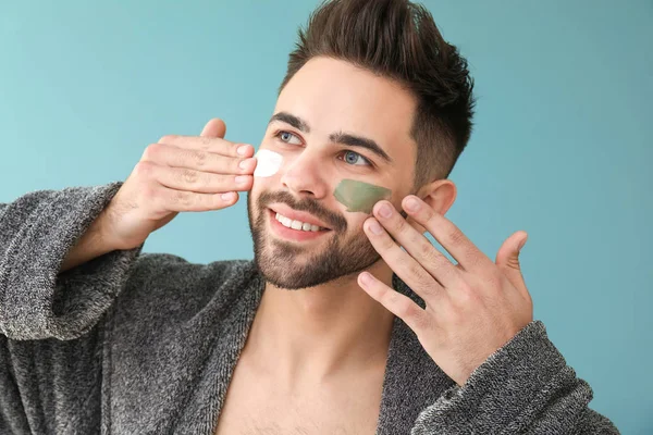 Handsome man applying clay mask on his face against color background — Stock Photo, Image