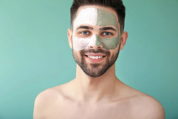 Hombre guapo con máscara de arcilla en su cara contra el fondo de color — Foto de Stock