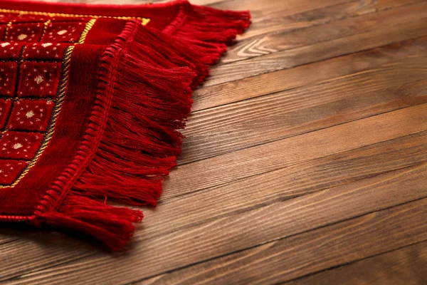 Muslim prayer rug on wooden background, closeup