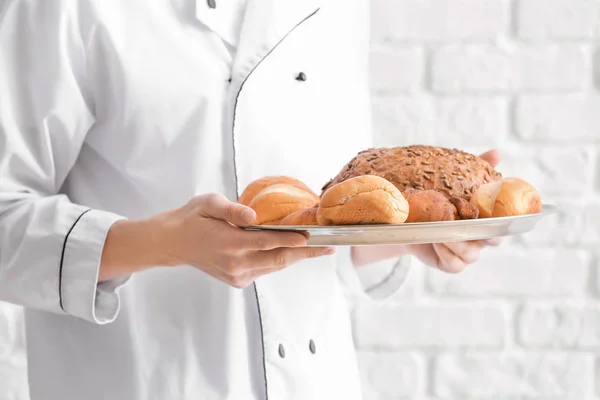 Young chef with fresh bakery products on white brick background, closeup