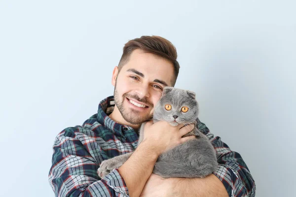 Young man with cute funny cat on light background — Stock Photo, Image