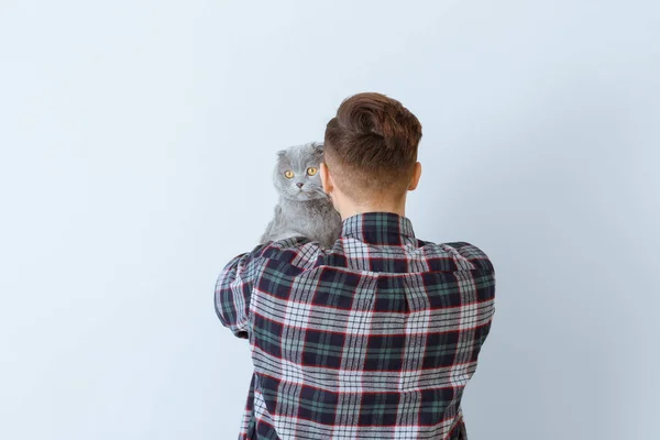 Young man with cute funny cat on light background — Stock Photo, Image