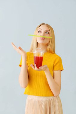 Funny young woman with fresh juice on light background