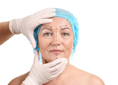 Beyaz arka plan üzerinde uygulanan işaretleri ile olgun kadının yüzüne dokunan plastik cerrah