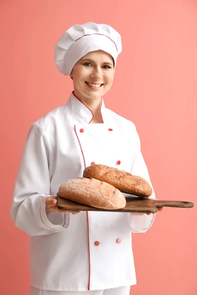Female baker with bread on color background