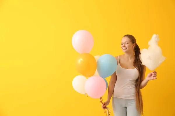 Hermosa mujer con algodón de azúcar y globos de aire sobre fondo de color — Foto de Stock