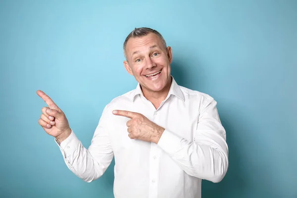 Happy middle-aged man pointing at something on color background — Stock Photo, Image