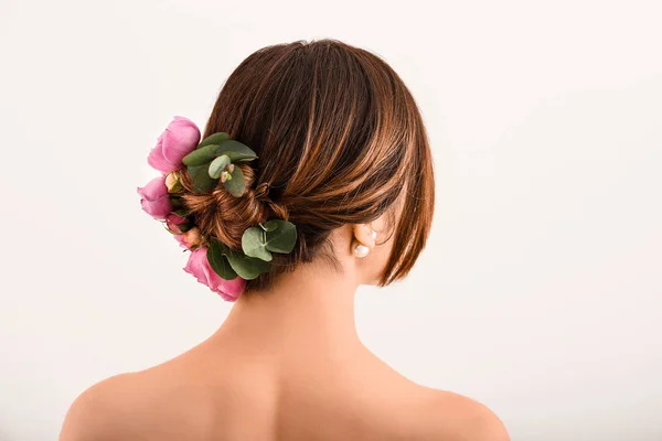 Jeune femme avec de belles fleurs dans ses cheveux sur fond clair, vue de dos — Photo