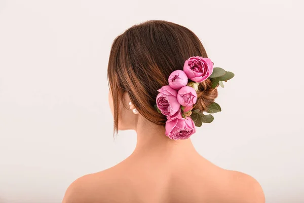 Jeune femme avec de belles fleurs dans ses cheveux sur fond clair, vue de dos — Photo