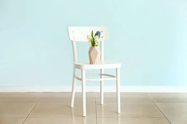 Vaso com belas flores de jacinto na cadeira contra a parede leve — Fotografia de Stock