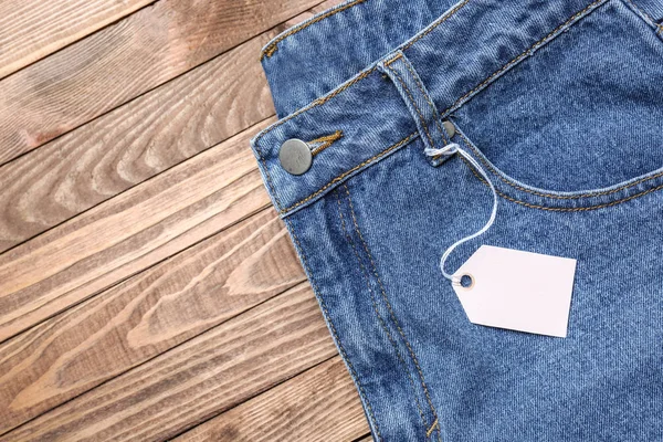 Calça jeans elegante com etiqueta no fundo de madeira — Fotografia de Stock