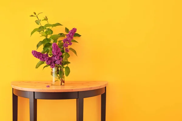 Красиві бузкові квіти у вазі на столі на кольоровому фоні — стокове фото