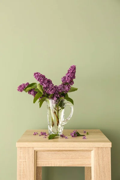 Красиві бузкові квіти в глечику на столі на кольоровому фоні — стокове фото