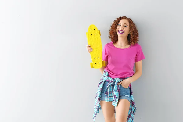 Stylish young woman with skateboard on light background — Stock Photo, Image