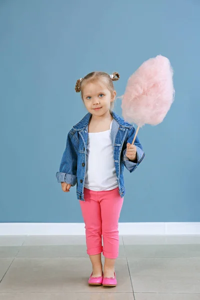 Cute little girl with cotton candy against color wall — Stock Photo, Image