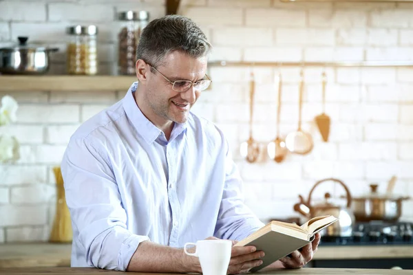 Yakışıklı olgun adam evde mutfakta kitap okuma — Stok fotoğraf