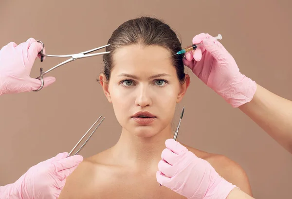 Mladá žena a ruce plastických chirurgů s nástroji na barevném pozadí — Stock fotografie