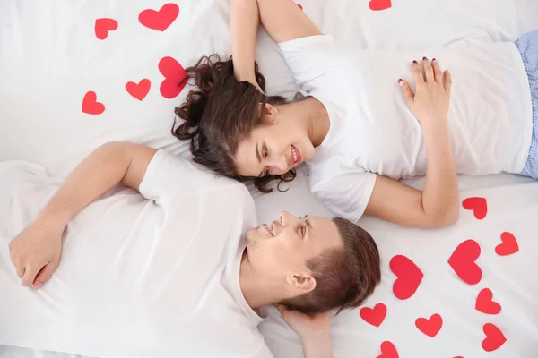 Feliz pareja joven con corazones de papel acostados en la cama —  Fotos de Stock