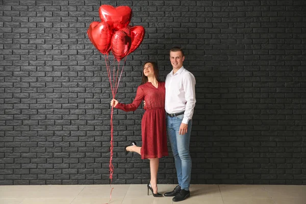 Счастливая молодая пара с воздушными шарами возле темной кирпичной стены — стоковое фото