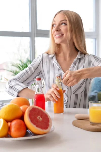 Hermosa joven con botellas de jugo fresco en casa — Foto de Stock