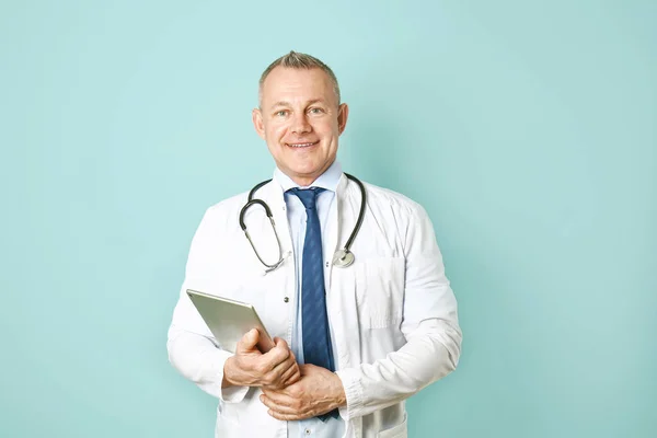 Handsome middle-aged doctor with tablet PC on color background — Stock Photo, Image