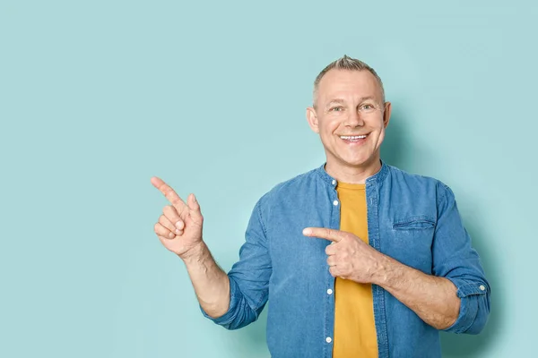 Portrait of handsome middle-aged man pointing at something on color background — Stock Photo, Image