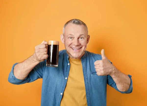 Happy middle-aged man with glass of beer showing thumb-up gesture on color background — Stock Photo, Image