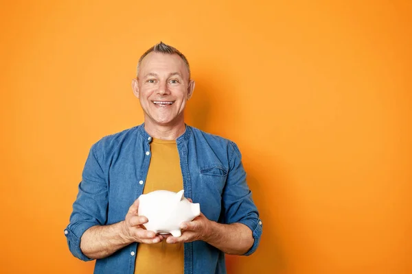 Handsome middle-aged man with piggy bank on color background — Stock Photo, Image