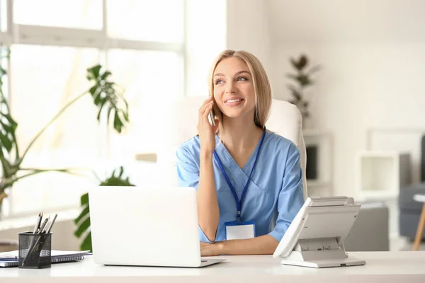 Жінка-медик розмовляє по телефону під час роботи на ноутбуці в клініці — стокове фото