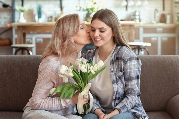 Filha feliz cumprimentando sua mãe com buquê de flores em casa — Fotografia de Stock