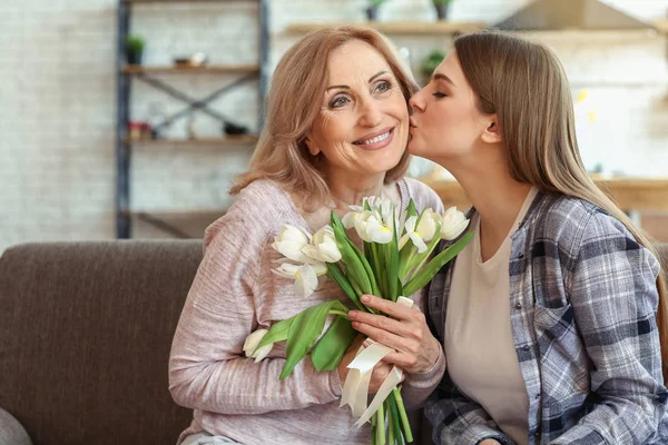 Happy daughter greeting her mother with bouquet of flowers at home — Stock Photo, Image