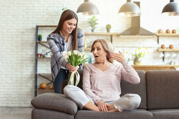 Happy daughter greeting her mother with bouquet of flowers at home — Stock Photo, Image