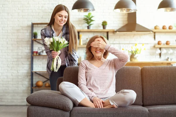 Happy daughter greeting her mother with bouquet of flowers at home — Stock Photo, Image