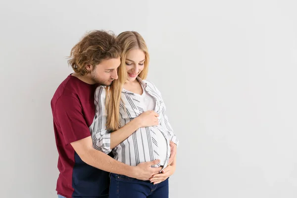 Happy young pregnant couple on light background — Stock Photo, Image