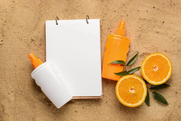 Crema de protección solar con cuaderno y fruta naranja sobre arena — Foto de Stock
